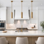 Symmetrical luxury modern kitchen with a white quartz island and three slim brushed brass cylinder pendant lights hanging evenly above in bright natural light