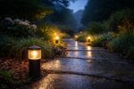 Atmospheric garden path at dusk illuminated by warm LED spike lights during rain, showing water droplets on outdoor ground lights, highlighting common outdoor lighting faults such as moisture ingress, condensation, and weather related performance issues.