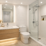 Small bathroom lighting with recessed downlights, a backlit mirror with vertical illumination, and subtle under vanity accent lighting, creating a bright, open, and airy feel in a compact space.